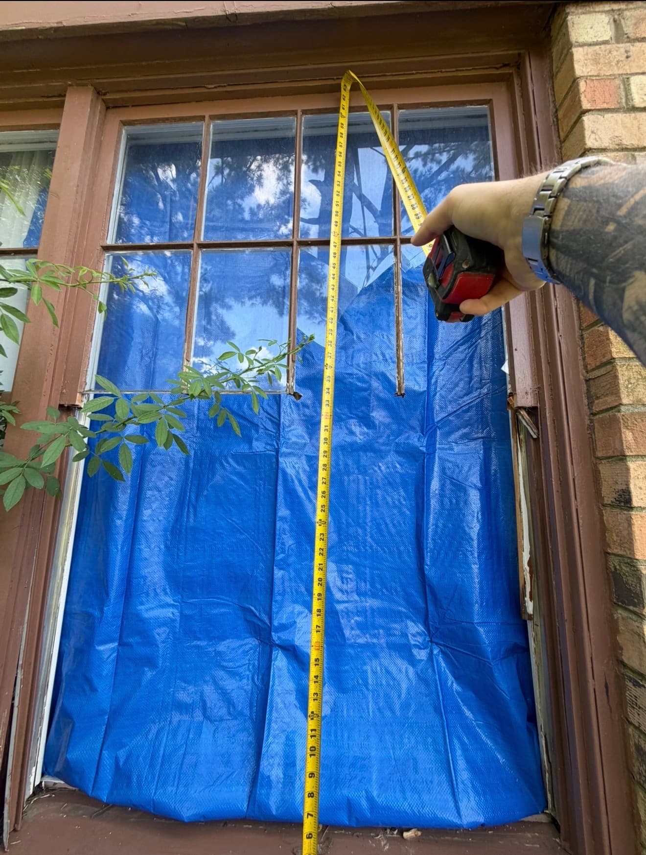 Emergency tarp over a storm-damaged window opening, measured for replacement