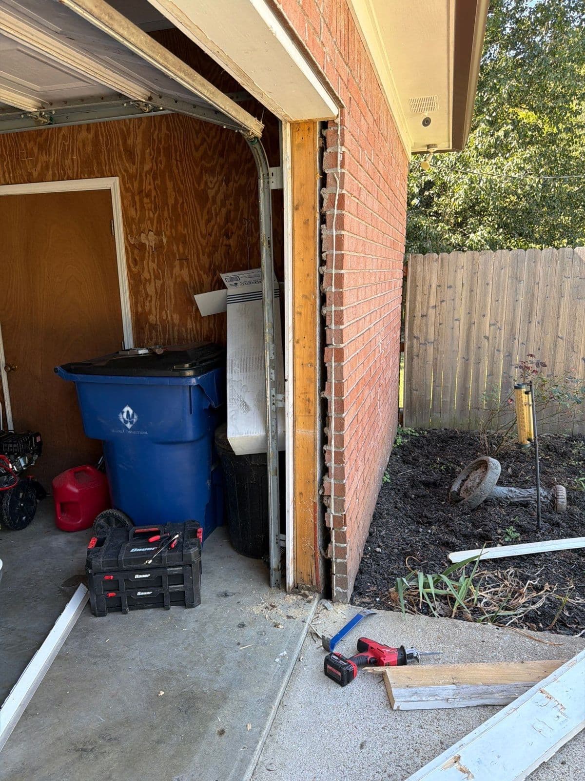 Rotted wood removed from the side of a garage door opening on a brick home, with the old boards on the driveway