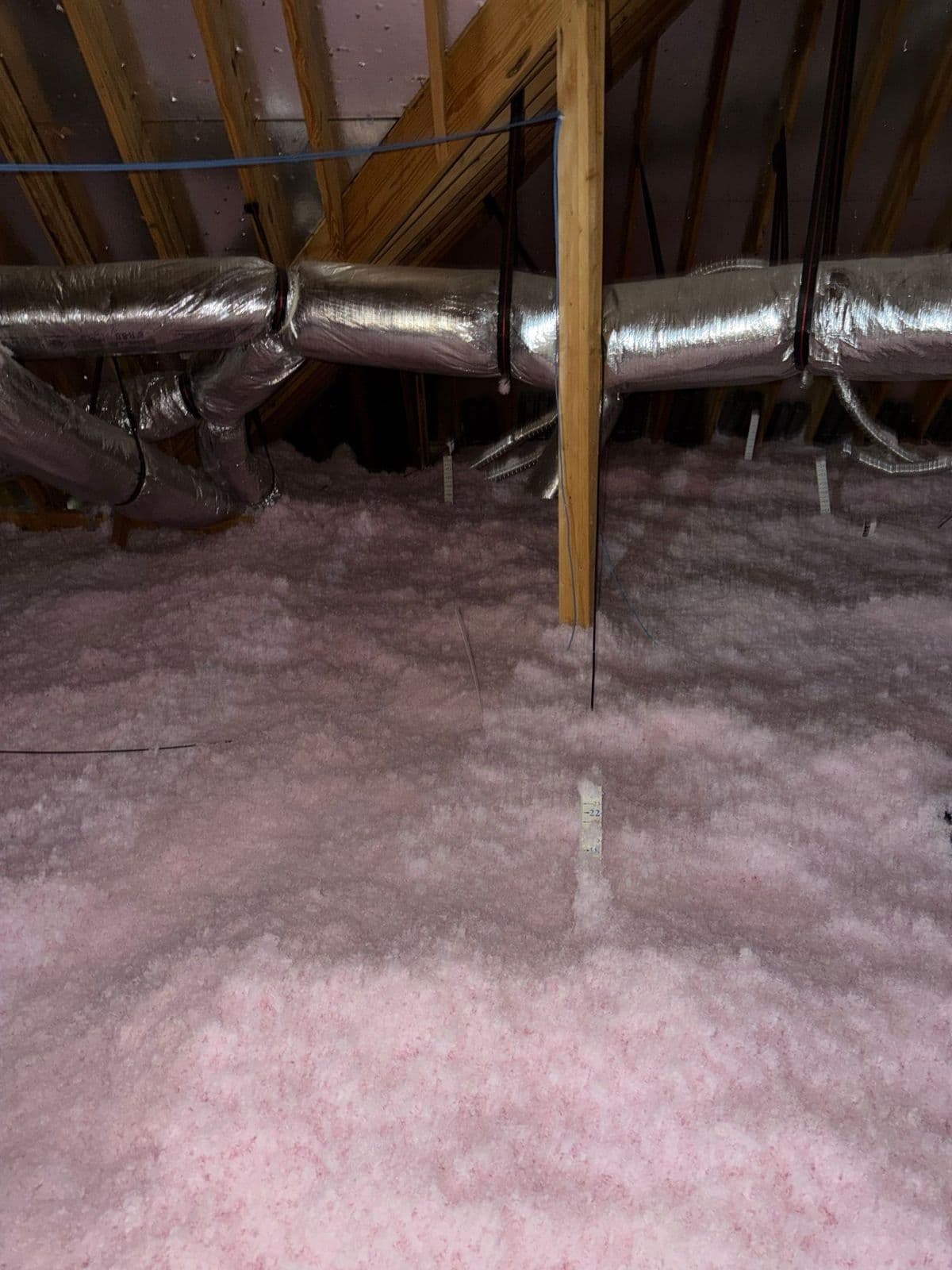 Attic with an even, deep layer of new pink fiberglass insulation under the ductwork
