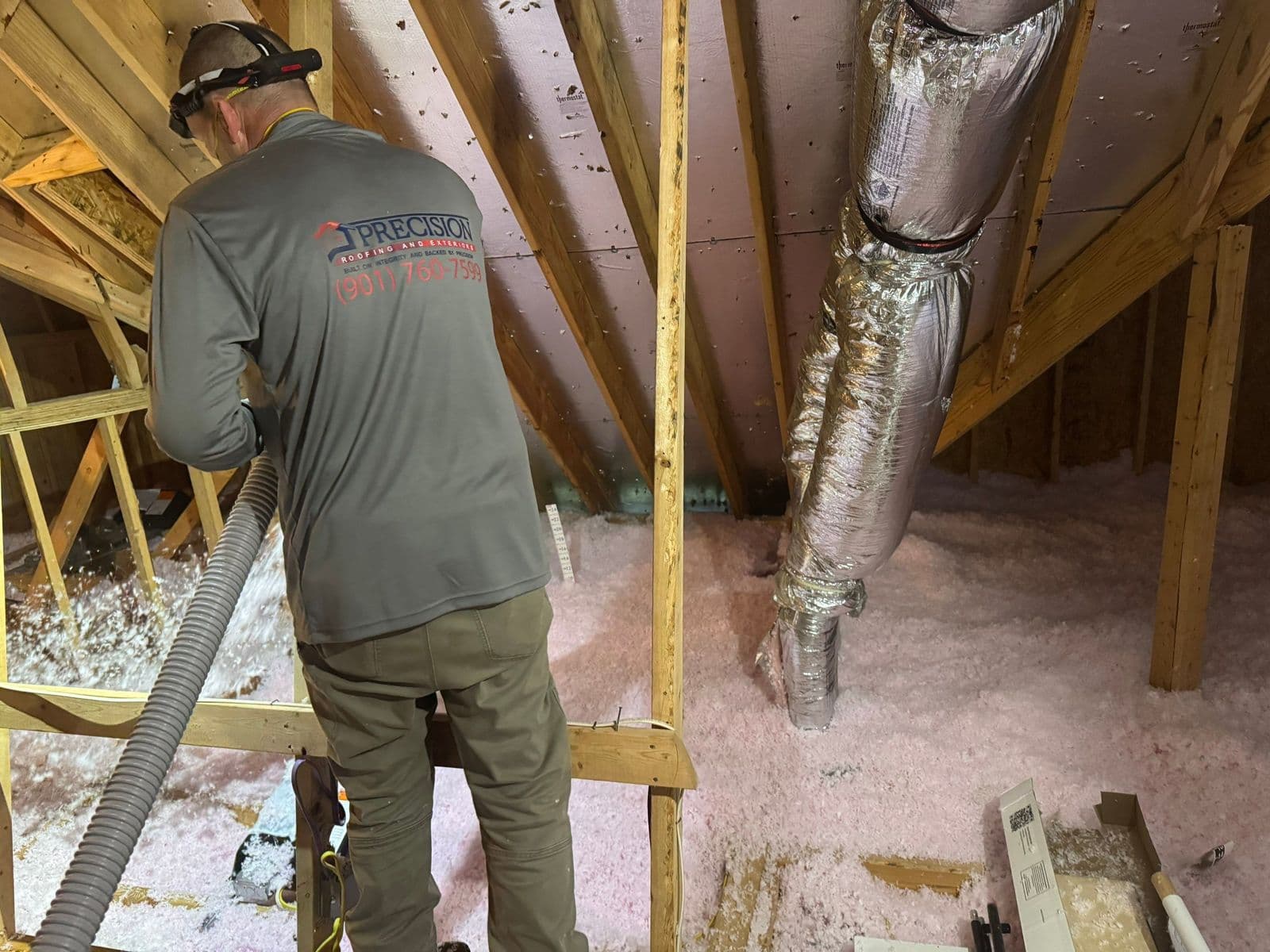 Precision Roofing crew member blowing pink fiberglass insulation across an attic floor