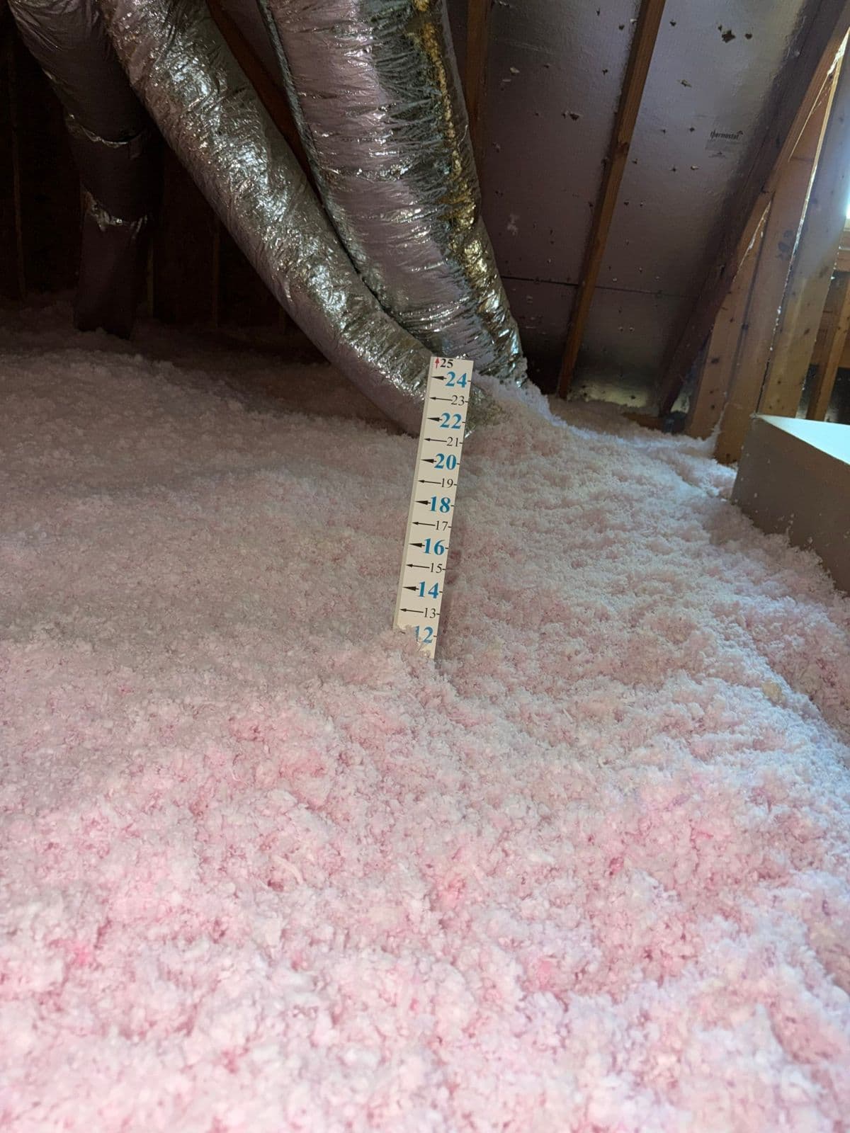 Depth ruler standing in deep new blown fiberglass insulation