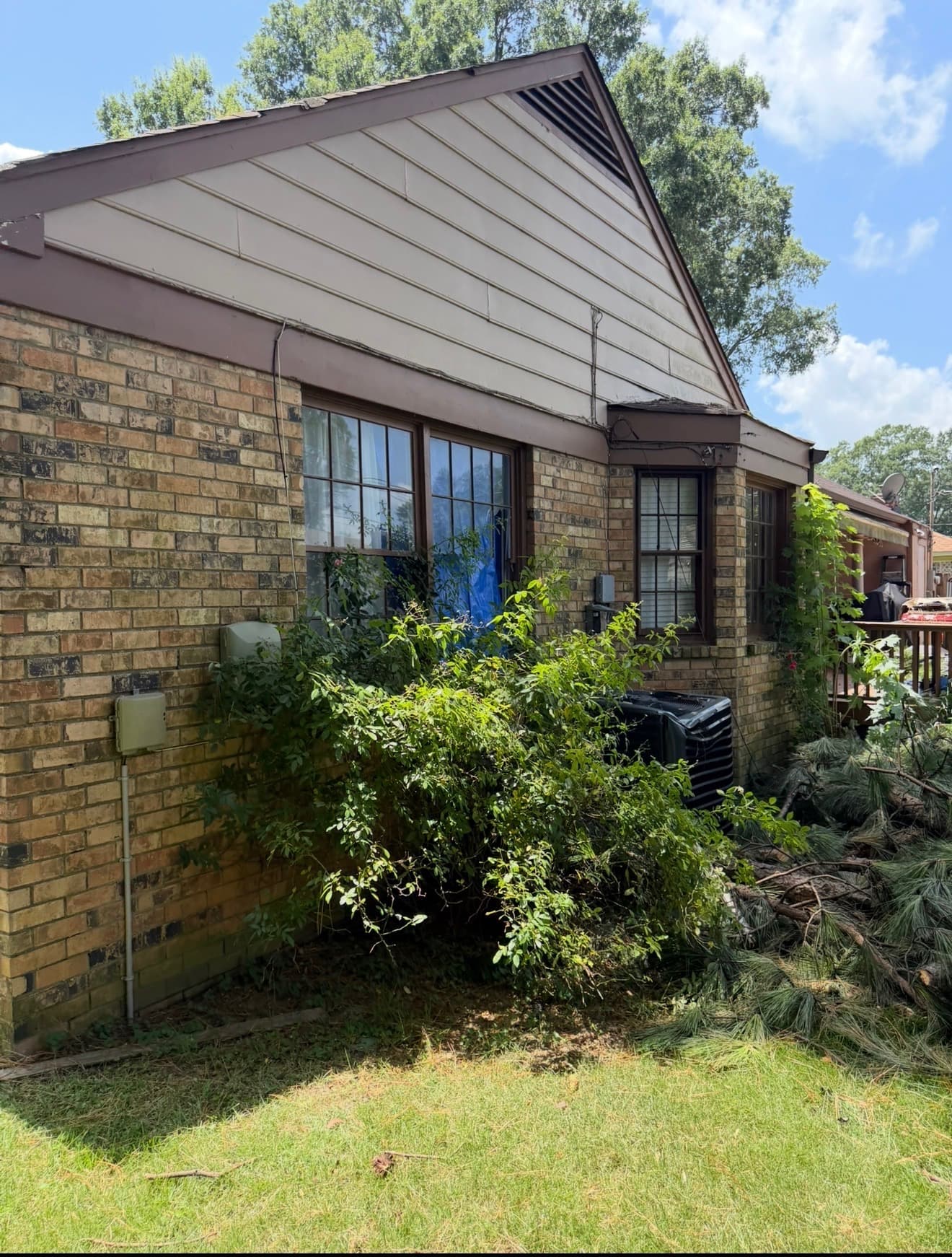 Side elevation of a brick home with a tarped window and storm debris in the yard