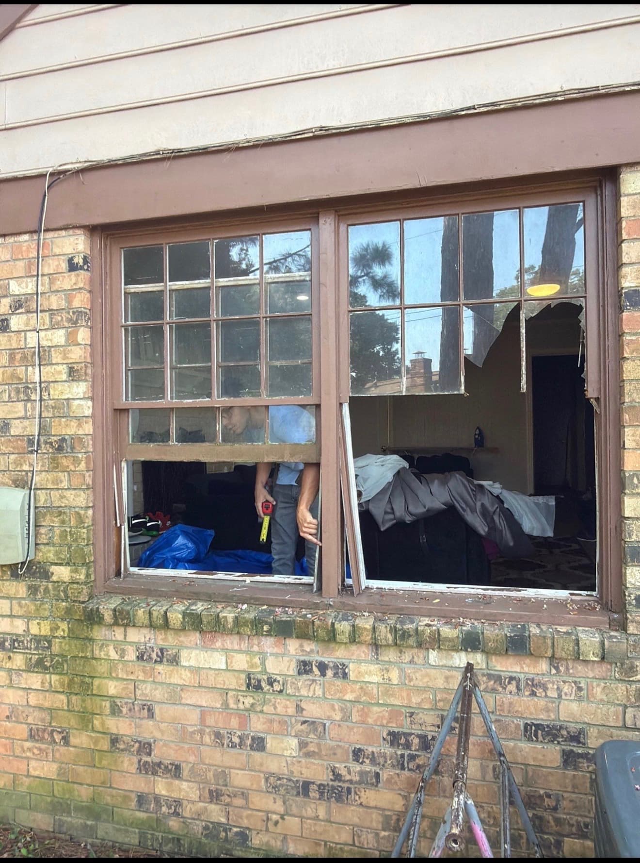 Old single-pane wood windows with broken glass being measured for replacement